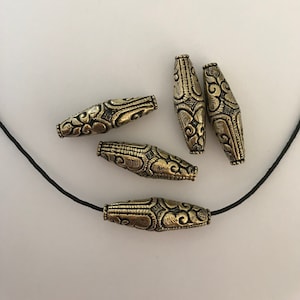May include: Five gold-toned metal beads with intricate floral designs. The beads are strung on a black cord.