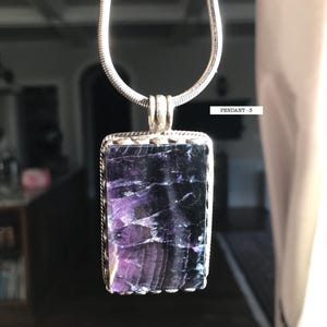 May include: A silver chain necklace with a rectangular pendant featuring a purple and blue fluorite stone. The pendant has a silver border with a scalloped edge. The text "PENDANT - 3" is visible in the image.