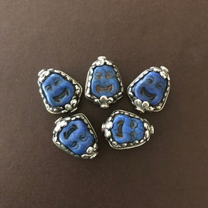 May include: Six blue and silver face beads with a smiling expression. The beads are shaped like a teardrop and have a silver trim.