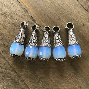 May include: Five silver teardrop-shaped pendants with opal stones. Each pendant has an ornate silver design.