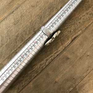 May include: A silver ring sizing tool with numbers from 5 to 36 marked on it. The tool is used to measure the size of a ring.