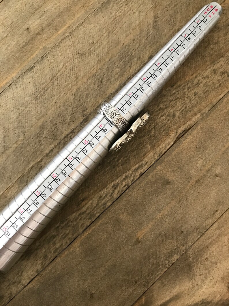 May include: A silver ring sizing tool with numbers from 5 to 36 marked on it. The tool is used to measure the size of a ring.