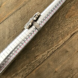 May include: A silver ring with a lizard design, measured on a ring sizer. The ring size is 19.
