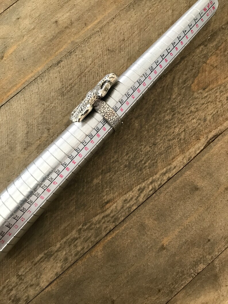May include: A silver ring with a lizard design, measured on a ring sizer. The ring size is 19.