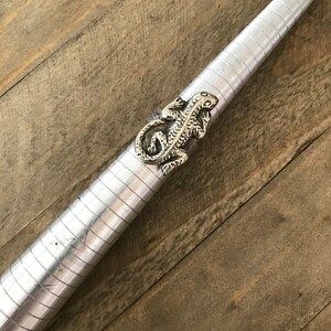 May include: A silver lizard ring on a metal ring sizer. The ring is detailed with scales and has a textured finish.