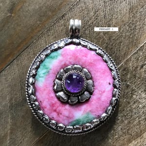May include: A silver pendant with a pink and green stone set in a silver flower design. The pendant has a purple amethyst stone in the center of the flower. The pendant is labeled "Pendant - 1".