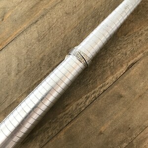May include: A silver ring sizing tool with a silver ring on it. The tool is made of metal and has a series of grooves that allow you to measure the size of a ring.