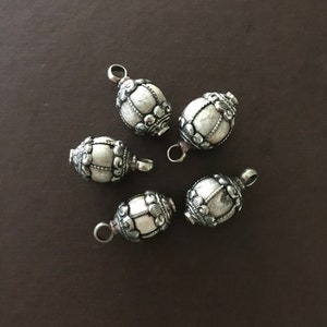 Puede incluir: Cinco cuentas de metal plateadas con diseños intrincados. Cada cuenta tiene un bucle en la parte superior para sujetar a un collar o pulsera.