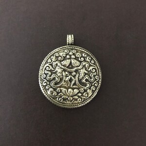 May include: A silver pendant featuring an intricate design with a floral motif and two stylised birds. The pendant is round and has a beaded edge.
