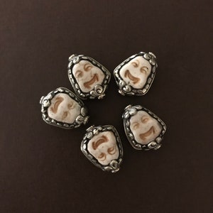 May include: Six silver and white face charm pendants with a detailed design. The charms are shaped like a teardrop and feature a smiling face.