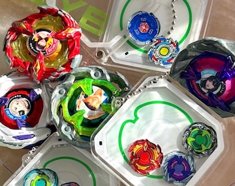 May include: A collection of Beyblade spinning tops in various colors including red, blue, green, and white, featuring character illustrations in the center. Several tops are stored inside clear, square plastic cases with green outlines.
