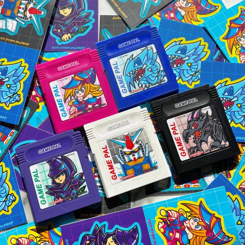 May include: A collection of colorful Game Pal video game cartridges. The cartridges are in various colors, including pink, blue, purple, white, and black. Each cartridge features a different anime-style character or robot illustration. The text "GAME PAL" is printed on each cartridge.