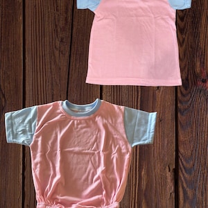 May include: Two pink and blue short-sleeved shirts. The top shirt is a t-shirt and the bottom shirt is a bodysuit.