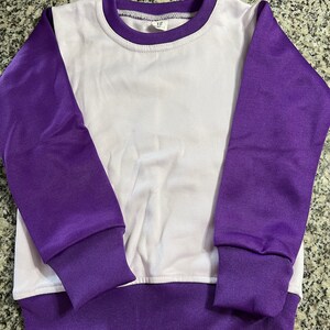 May include: A white and purple sweatshirt. The long sleeves, collar, and hem are purple, while the body is white. The cuffs and hem are ribbed. The crew neck sweatshirt is designed for comfort and style.