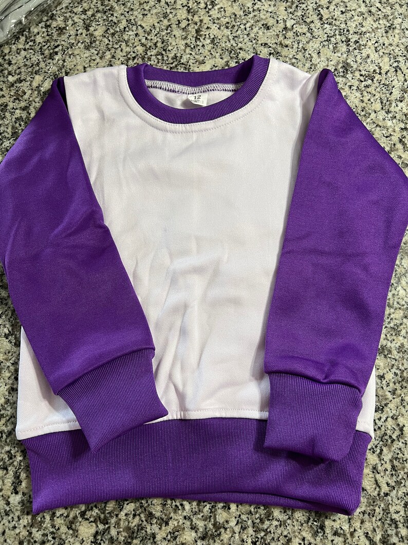 May include: A white and purple sweatshirt. The long sleeves, collar, and hem are purple, while the body is white. The cuffs and hem are ribbed. The crew neck sweatshirt is designed for comfort and style.