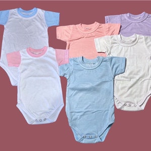 May include: Five baby onesies in different colors. The onesies are white, light blue, pink, lavender, and a white onesie with pink and blue trim. The onesies have short sleeves and snap closures.