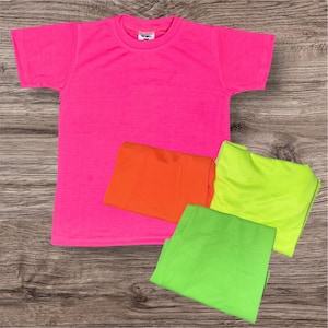 May include: A bright pink short-sleeved t-shirt is displayed with three folded shirts in orange, neon green, and green. The shirts are arranged on a wooden surface, showcasing a vibrant color palette.
