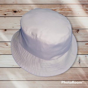 May include: A plain white bucket hat. The hat is made of a soft, lightweight fabric. It has a wide brim and a flat crown.