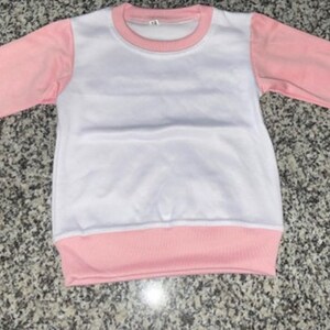 May include: A white and pink long-sleeved sweatshirt. The sleeves and the bottom hem are a soft pink, while the body is white. The neckline is also pink. The garment is made of a soft material.