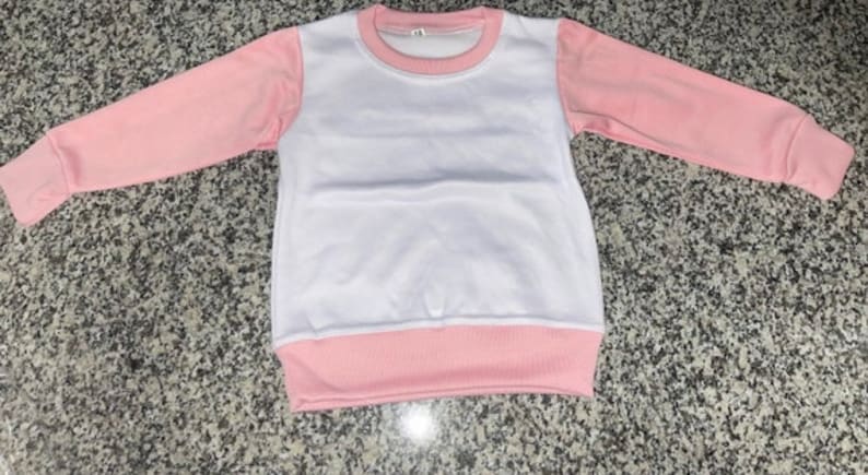 May include: A white and pink long-sleeved sweatshirt. The sleeves and the bottom hem are a soft pink, while the body is white. The neckline is also pink. The garment is made of a soft material.