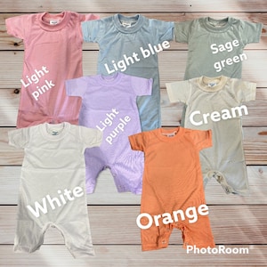 May include: Seven baby onesies in different colors: light pink, light blue, sage green, cream, light purple, white, and orange. The onesies are laid out on a wooden surface.