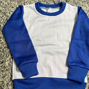 May include: A white and blue sweatshirt with a crew neck. The sleeves and bottom hem are blue, and the body is white. The neckline is trimmed with blue. The tag reads "12 months".