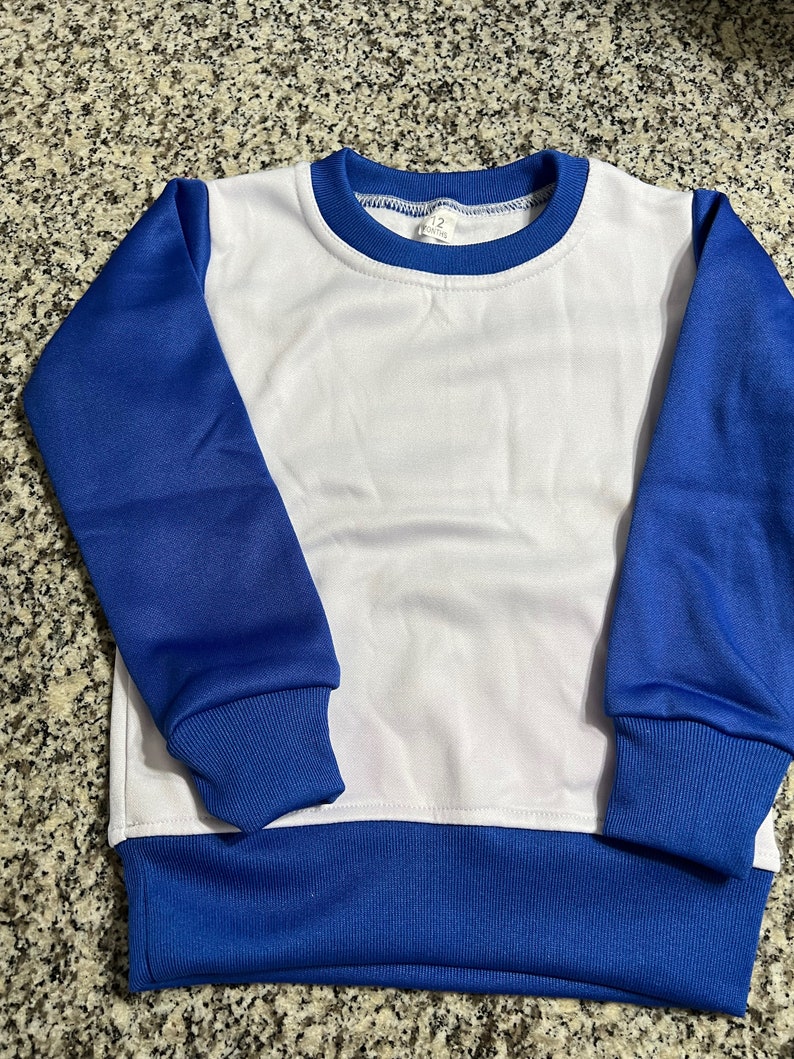May include: A white and blue sweatshirt with a crew neck. The sleeves and bottom hem are blue, and the body is white. The neckline is trimmed with blue. The tag reads "12 months".