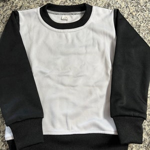 May include: A white and black sweatshirt with a crew neck and long sleeves. The body of the sweatshirt is white, while the sleeves, collar, and hem are black. The tag reads "12 months".