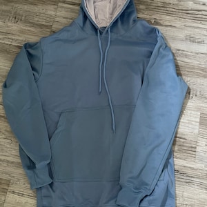 Op de afbeelding: Een lichtblauw hoodie met een zak en een capuchon met trekkoord.