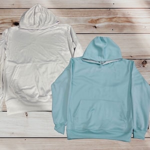 May include: Two hooded sweatshirts, one white and one light blue, laid out on a wooden surface.