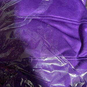 Op de afbeelding: Een paarse hoodie met een wit label waarop "XL" staat. De hoodie is verpakt in plastic.