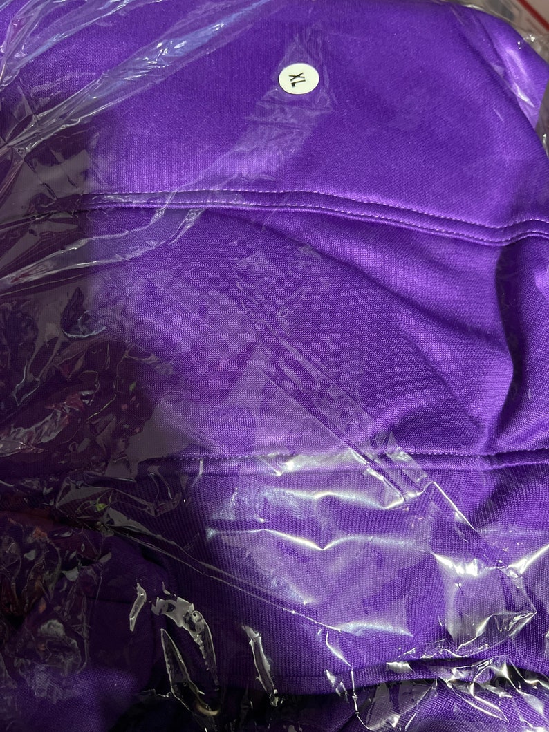 Op de afbeelding: Een paarse hoodie met een wit label waarop "XL" staat. De hoodie is verpakt in plastic.