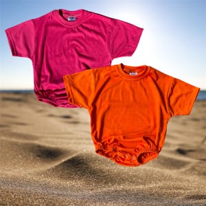 May include: Two short-sleeved baby bodysuits. One is a vibrant fuchsia pink, and the other is a bright orange. Both have a round neckline and a gathered bottom with snap closures. The background is a beach scene.