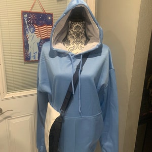 Op de afbeelding: Een lichtblauw hoodie met een witte voering en een zwart-witte schoudertas.