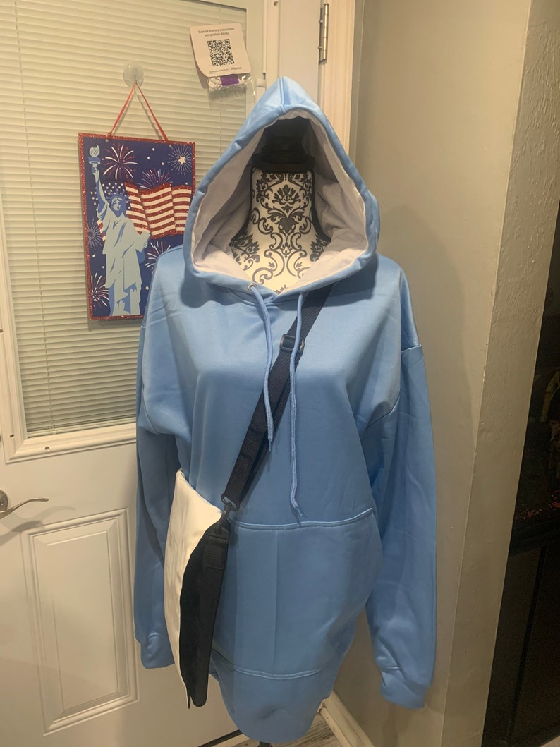 Op de afbeelding: Een lichtblauw hoodie met een witte voering en een zwart-witte schoudertas.