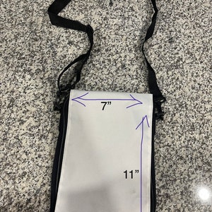 May include: A white canvas crossbody bag with black trim. The bag measures 11 inches tall and 7 inches wide.