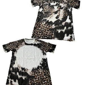 Könnte beinhalten: Ein weißes T-Shirt mit einem schwarzen, braunen und weißen Leopardenmuster. Das Shirt hat kurze Ärmel und einen Rundhalsausschnitt.