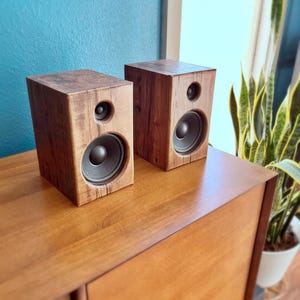 Può includere: Una coppia di altoparlanti rettangolari da scaffale con casse in legno marrone scuro. Ogni unità altoparlante contiene un woofer circolare grande e un tweeter circolare più piccolo posizionato sopra, entrambi con coni neri.