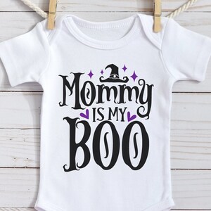 May include: White baby onesie with black text that reads "Mommy is my Boo" with a purple witch hat and stars above the text.