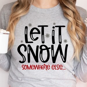 May include: A gray sweatshirt with the text "Let it snow somewhere else..." in black and red lettering. The text is surrounded by small white stars.