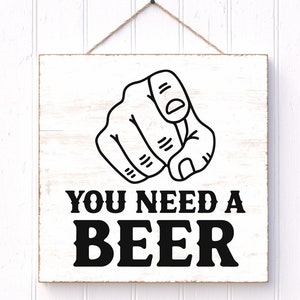 May include: A white wooden sign with a black and white illustration of a pointing finger and the text "YOU NEED A BEER".