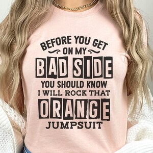 May include: A pink t-shirt with black text that reads "Before you get on my bad side you should know I will rock that orange jumpsuit".