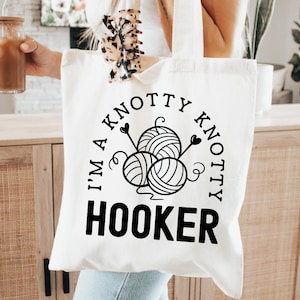 May include: White tote bag with black text that reads "I'm a knotty knotty hooker" with a graphic of yarn balls and needles.