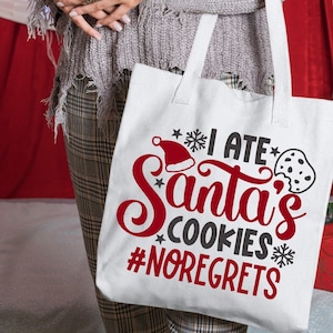 May include: White tote bag with the text "I ate Santa's cookies #noregrets" in red and black lettering. A red Santa hat and a black and white cookie are also included in the design.