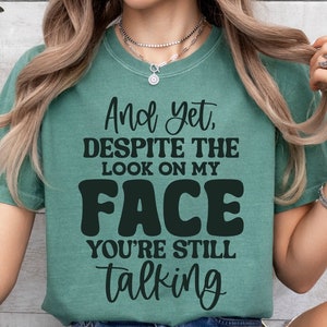 May include: A teal green t-shirt with the text "And yet, DESPITE THE LOOK ON MY FACE YOU'RE STILL talking" in black.