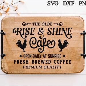 Könnte beinhalten: Ein Holzschild mit schwarzem Text, der "The Olde Rise & Shine Cafe" mit zwei Hahnensilhouetten lautet. Das Schild sagt auch "Täglich bei Sonnenaufgang geöffnet", "Frisch gebrühter Kaffee" und "Premiumqualität".