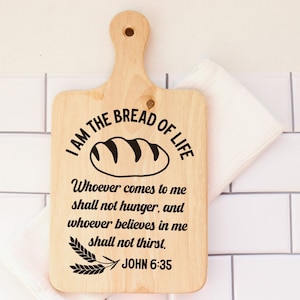 May include: A wooden cutting board with a handle, featuring the text "I am the bread of life" and a loaf of bread illustration. The text below the illustration reads "Whoever comes to me shall not hunger, and whoever believes in me shall not thirst. John 6:35".