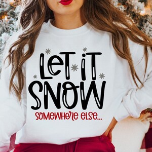 May include: White sweatshirt with black text that reads "Let it snow somewhere else..." with small gray snowflakes around the text.