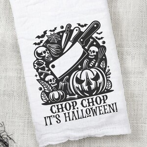 Könnte beinhalten: Ein schwarz-weißes Küchentuch mit einem Halloween-Motiv. Das Design zeigt ein Metzgermesser, einen Kürbis und Schädel. Der Text "Chop, Chop It's Halloween!" ist auf das Handtuch gedruckt.