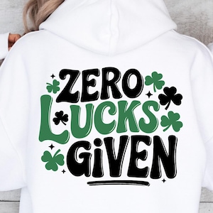Op de afbeelding: Witte hoodie met een zwarte en groene afbeelding met de tekst "Zero Lucks Given" met klavertje vier designs.